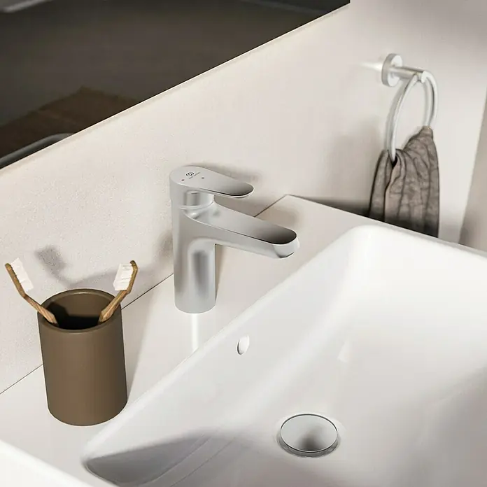 Ideal Standard Alu+ Waschtischarmatur - Höhe: 160 cm, Silber - Moderner silberner Wasserhahn auf einem weißen Waschbecken, mit Zahnbürsten und Handtuch.
