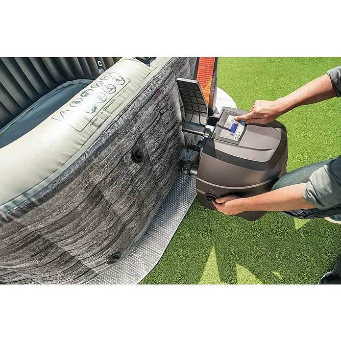 Intex Pure Spa Mobil-Whirlpool Greystone Deluxe - L x B x H: 196 x 196 x 71 cm, Grau, 1.098 l - Hände bedienen ein dunkelgraues Steuergerät, das mit einem aufblasbaren grauen Whirlpool verbunden ist.