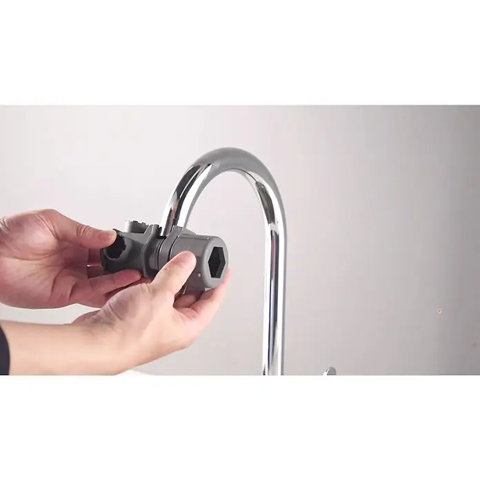 Llave de tubo - Largo: 100 mm, Plástico, Número de aplicaciones: 16 ud. - Manos sosteniendo una multiherramienta gris con apertura hexagonal, cerca de un grifo cromado para instalación o ajuste.