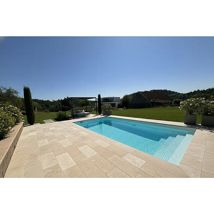 Mountfield Bausatz-Pool - L x B x H: 650 x 350 x 150 cm, 23,83 m³, Weiß - Helle Steinoptik-Pflasterplatten schaffen eine einladende, geräumige Terrasse um einen modernen Rechteckpool an einem sonnigen Tag.