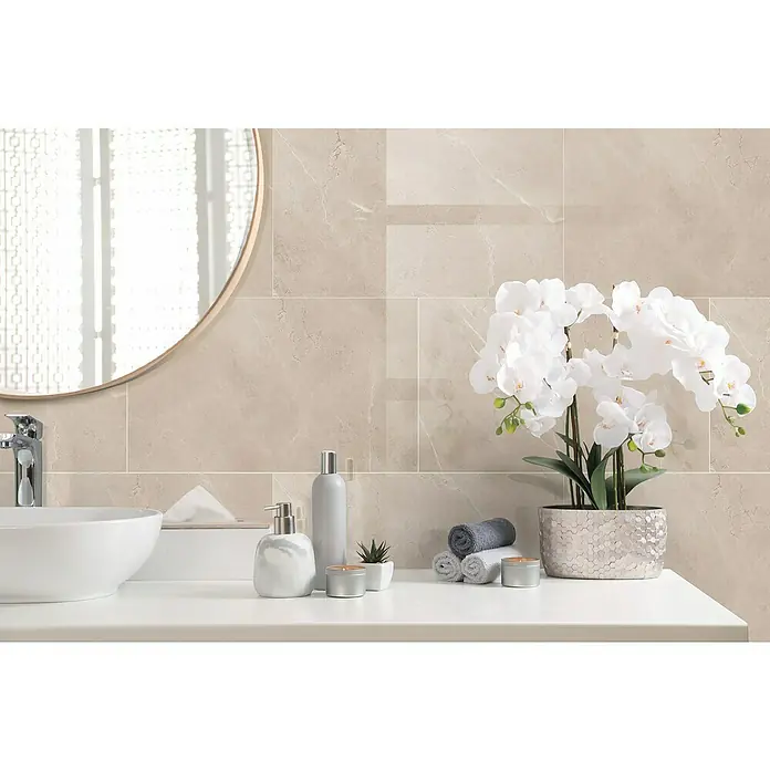 Dumawall+ Revestimiento de pared de PVC Gust Gloss - 75 x 45 cm, Beige - Azulejos de aspecto mármol beige claro en una pared de baño, creando un fondo sereno y elegante para un tocador con lavabo y decoración.