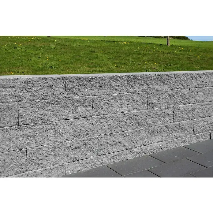 Christoph Mauerstein Rustikalblock - 50 x 12,5 x 14 cm, Kristall/Grau, Beton - Graue, strukturierte Blocksteinmauer, die einen grünen Hang von einem gepflasterten Bereich trennt.