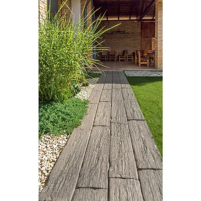 EHL Trittstein Bahnschwelle - 90 x 22,5 x 5 cm, Braun, Beton - Gartenweg aus Holzoptik-Platten führt zu einer Terrasse, flankiert von Pflanzen und Kieselsteinen.