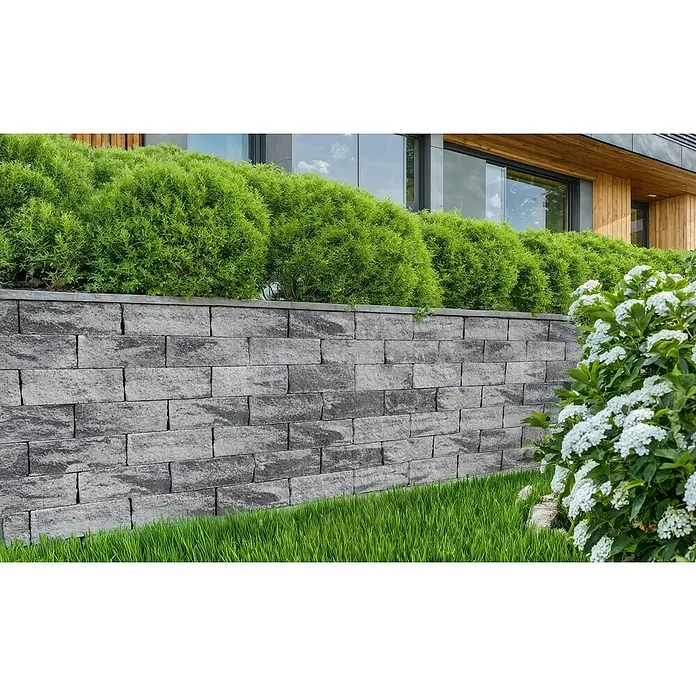 EHL EIBA Mauerstein - 60 x 15 x 12 cm, Grau-Anthrazit, Beton - Graue modulare Block-Stützmauer, die grüne Büsche und einen Garten neben einem modernen Gebäude stützt.