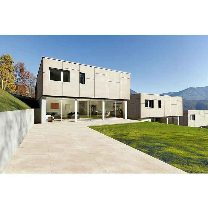 Terrassenfliese Colosseo - 120 x 120 x 2 cm, Pietra, Matt - Helle, strukturierte Außenfliesen bilden eine Terrasse und einen Weg um ein modernes Haus mit Rasen.