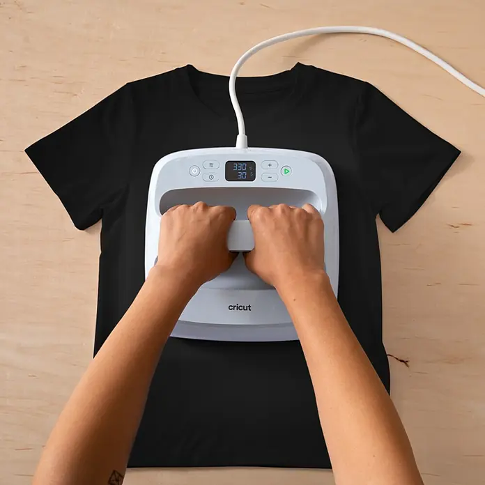 Cricut Aufbügelfolie Bedruckbares Iron-On - 29,7 x 21 cm, Passend für: Dunkle Stoffe, 3 Stk. - Hände drücken eine weiße Cricut Heizpresse auf ein schwarzes T-Shirt; Display zeigt 330°F und 30s.