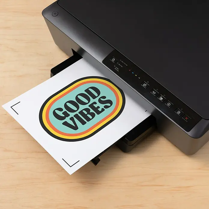 Cricut Aufbügelfolie Bedruckbares Iron-On - 29,7 x 21 cm, Passend für: Dunkle Stoffe, 3 Stk. - Schwarzer Drucker druckt ein weißes Blatt Papier mit einem farbigen „GOOD VIBES“-Design.