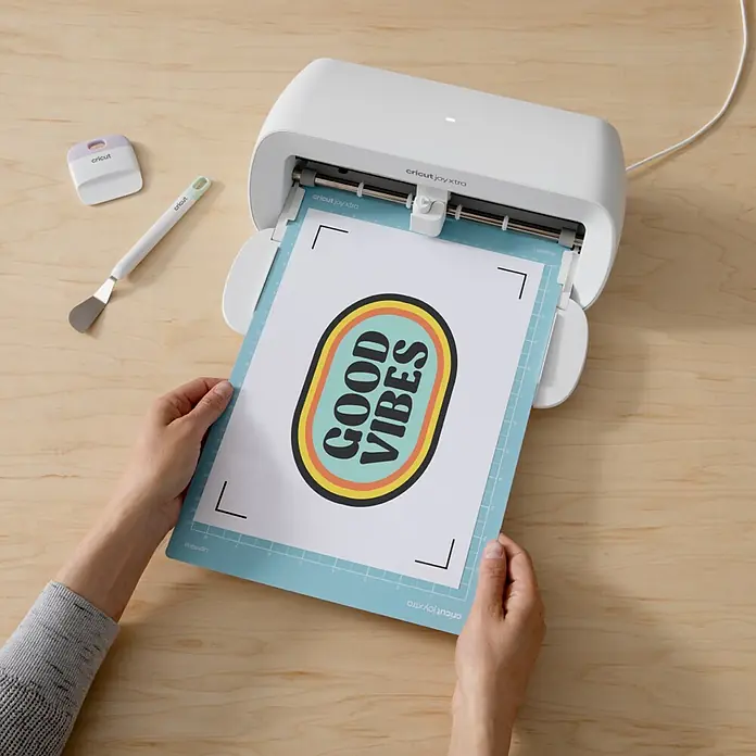 Cricut Aufbügelfolie Bedruckbares Iron-On - 29,7 x 21 cm, Passend für: Dunkle Stoffe, 3 Stk. - Weiße Cricut Joy Xtra Maschine, die eine Matte mit "GOOD VIBES"-Design zum Schneiden einzieht.