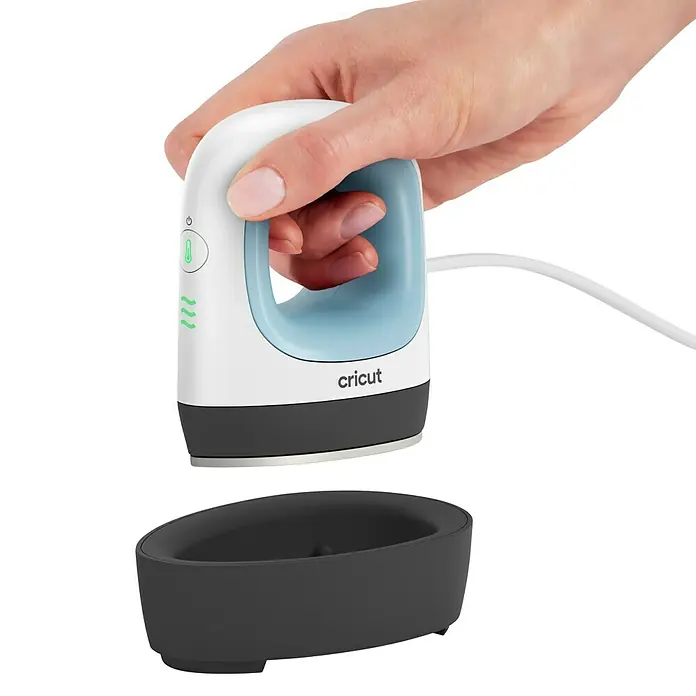 Cricut Transferpresse EasyPress Mini - Passend für: Bügelfolien, Drucktechnologie: Wärmeübertragung - Hand hält weiß/hellblauen Cricut EasyPress Mini über dunkelgrauer Sicherheitsbasis.
