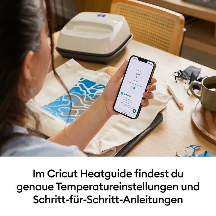 Cricut Transferpresse EasyPress SE + Hitzeschutzmatte - 22,5 x 22,5 cm, Passend für: Bügelfolien - Eine Person hält ein Telefon mit Anleitungen des Cricut Heat Guide für ein Transferprojekt, mit einer EasyPress daneben.
