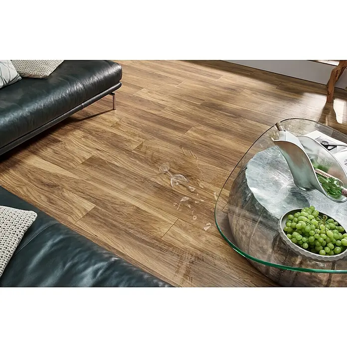 LOGOCLIC Vinto Laminat - Marsala, Landhausdiele, 1.288 x 195 x 10 mm - Helles Holzparkett im Wohnzimmer, mit verschüttetem Wasser und zerbrochenem Glas neben einem Sofa.