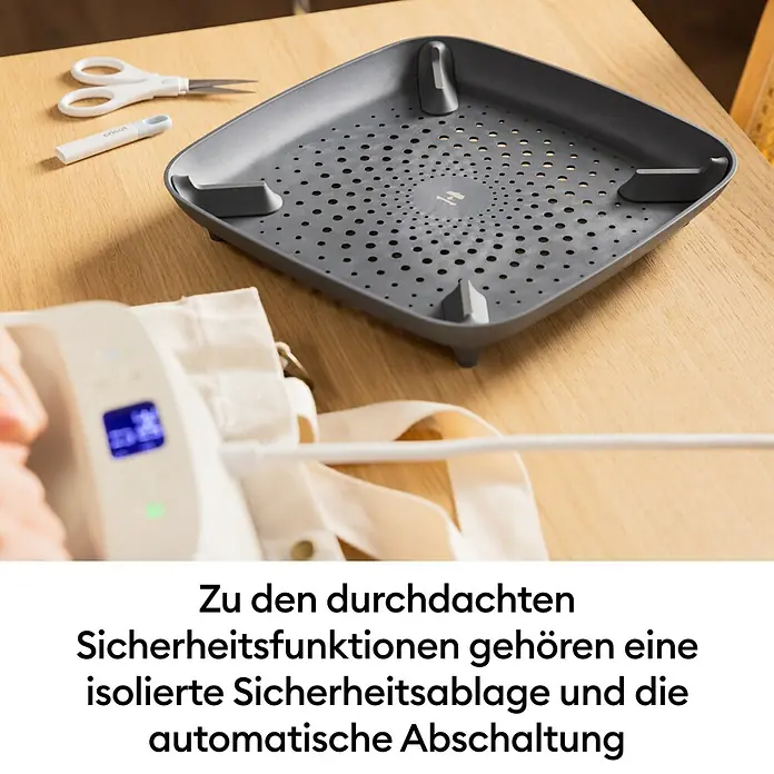 Cricut Transferpresse EasyPress SE + Hitzeschutzmatte - 22,5 x 22,5 cm, Passend für: Bügelfolien - Eine graue, quadratische, perforierte Sicherheitsablage für eine Heizpresse auf einem Holztisch, mit Werkzeugen daneben.