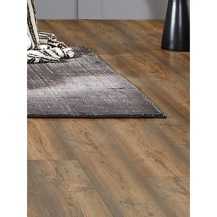 LOGOCLIC Vinto Laminat - Eiche Bergamo, Landhausdiele, 1.288 x 195 x 8 mm - Dunkelgrauer, strukturierter Teppich mit dezentem Streifenmuster, auf warmbraunem Holzboden.