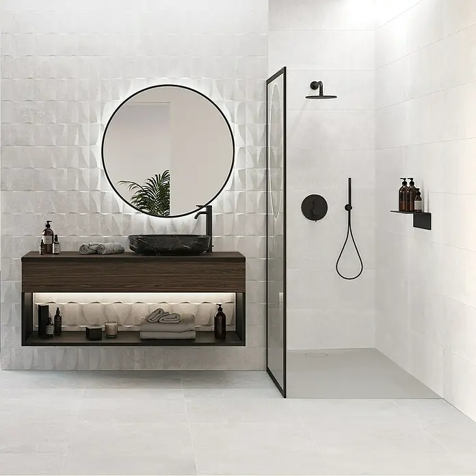 Revestimiento de pared Brikston - 30 x 90 cm, Blanco, Rectificado - Baño moderno: mueble de baño madera oscura, lavabo piedra negra, espejo redondo retroiluminado, ducha con grifería negra, azulejos claros texturizados.