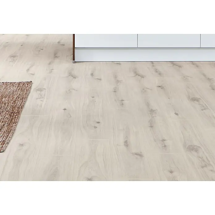 LOGOCLIC Aquaprotect Laminat - Beach Oak, Landhausdiele, 1.288 x 195 x 8 mm - Heller Laminatboden mit natürlicher Holzmaserung, der sich von einem braunen Teppich bis unter einen weißen Küchenunterschrank erstreckt.