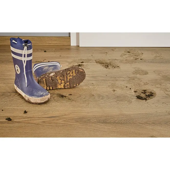 LOGOCLIC Vinto Laminat - Eiche Kronos, Landhausdiele, 1.288 x 195 x 10 mm - Schlammige blaue Gummistiefel mit weißen Streifen auf Holzboden mit Schlammspritzern.