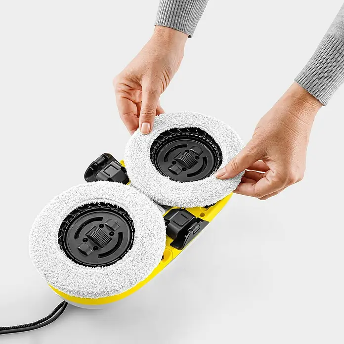 Kärcher Fensterreinigungsroboter RCW 2 - Wassertankvolumen Roboter: 70 ml, Saugkraft: 3.300 Pa - Hände befestigen weiße Mikrofaser-Reinigungspads an den schwarzen Antriebsköpfen eines gelb-schwarzen Kärcher Bodenreinigers.