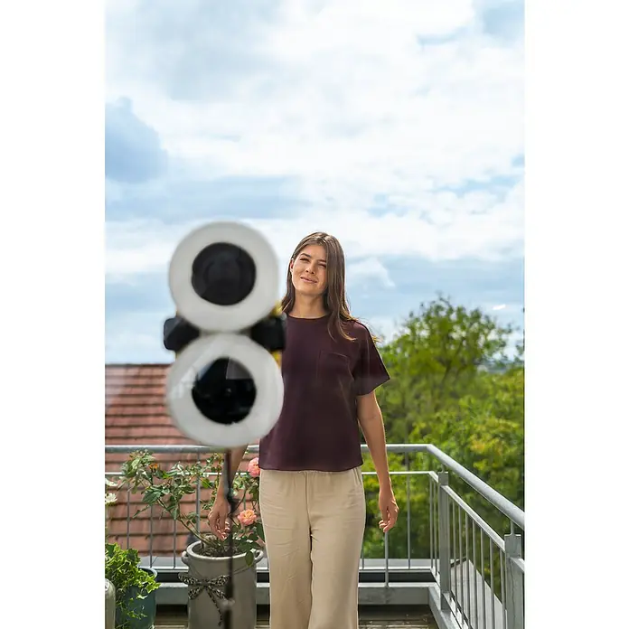 Kärcher Fensterreinigungsroboter RCW 2 - Wassertankvolumen Roboter: 70 ml, Saugkraft: 3.300 Pa - Frau trägt bordeauxrotes Kurzarm-Oberteil mit Tasche und hellbeige weite Hose auf einem Balkon.