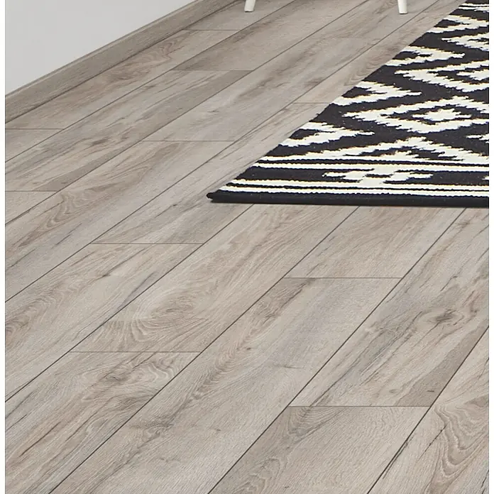 LOGOCLIC Aquaprotect Smart Laminat - Eiche Lucha, Landhausdiele, 1.288 x 195 x 6 mm - Hellgrauer Laminatboden mit sichtbarer Holzmaserung, teilweise bedeckt von einem schwarz-weiß gemusterten Teppich.