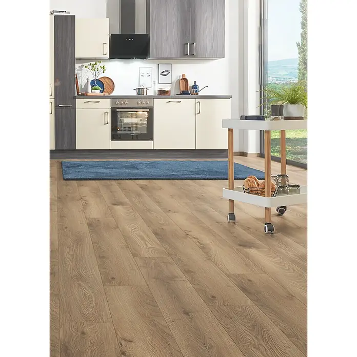 LOGOCLIC Aquaprotect Smart Silent Laminat - Ringa Oak, Landhausdiele, 1.288 x 195 x 7 mm - Hellbrauner Laminatboden in Holzoptik in einer modernen Küche, mit blauem Teppich und weißem Servierwagen.