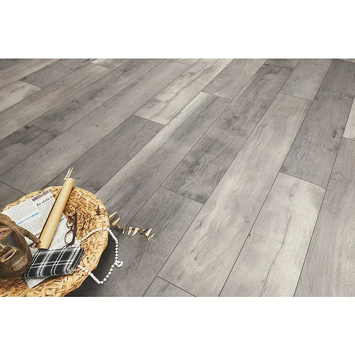 LOGOCLIC Aquaprotect Laminat - Tasso Oak, Landhausdiele, 1.288 x 245 x 8 mm - Grauer Laminatboden in Holzoptik in einem Raum verlegt, mit einem dekorativen Korb im Vordergrund.
