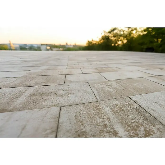 EHL Terrassenplatte Olinda - 40 x 40 x 4 cm, Sandstein, Beton - Helle beige, rechteckige Pflasterfliesen mit melierter Textur auf einer Außenterrasse, mit verschwommener Landschaft bei Sonnenuntergang.