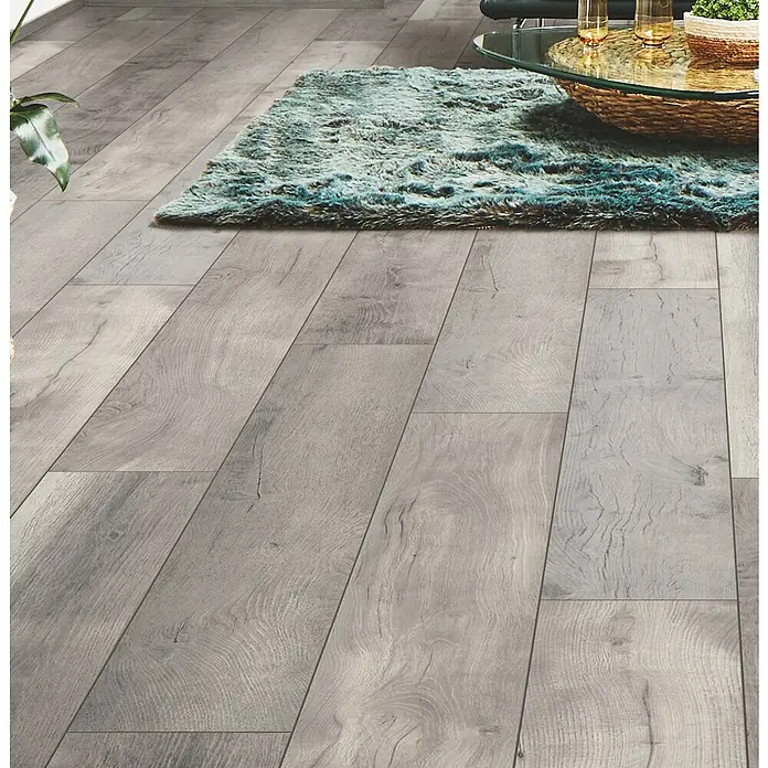 LOGOCLIC Aquaprotect Laminat - Tasso Oak, Landhausdiele, 1.288 x 245 x 8 mm - Grauer Holzplankenboden in einem Raum, teilweise von einem strukturierten Teppich bedeckt.