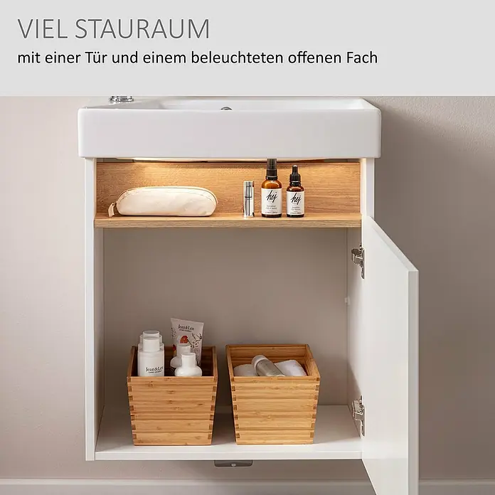 Camargue Pure Badmöbel-Set - Gesamtbreite Badmöbel: 55 cm, Weiß/Eiche, Matt - Weißer Waschtischunterschrank mit beleuchtetem offenem Holzfach und geschlossenem Stauraum mit Tür, gefüllt mit Kosmetik.