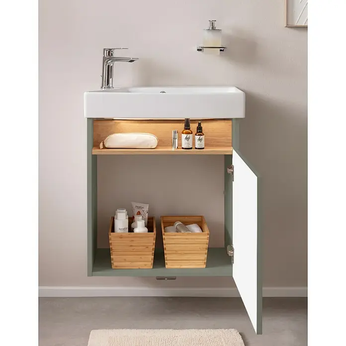 Camargue Pure Badmöbel-Set - Gesamtbreite Badmöbel: 55 cm, Salbeigrün, Matt - Eine wandmontierte salbeigrüne Badmöbel mit weißem Waschbecken, einem beleuchteten Holzregal und einem offenen Schrank mit Holz-Aufbewahrungskörben.