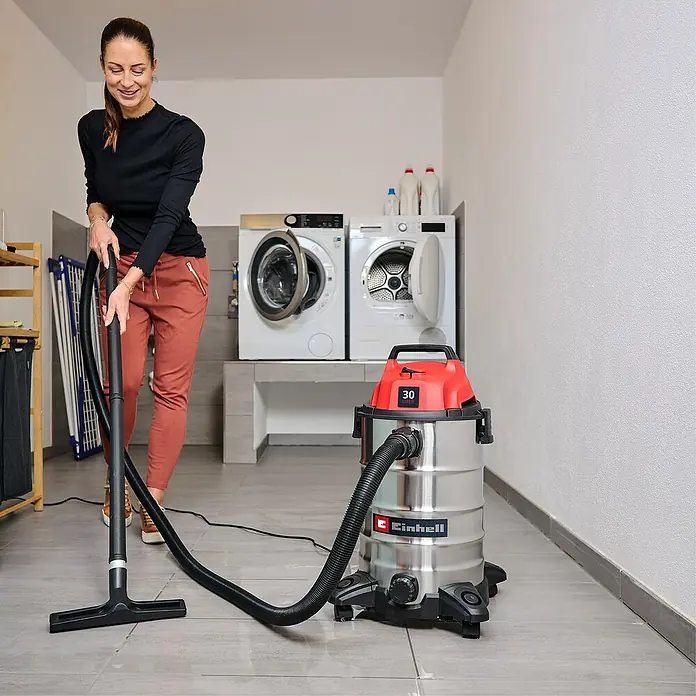 Einhell Nass-Trockensauger TC-VC 3055 S - 950 W, 30 l - Eine Frau saugt mit einem rot-silbernen Einhell Nass-Trocken-Sauger den Boden in einem Waschraum.
