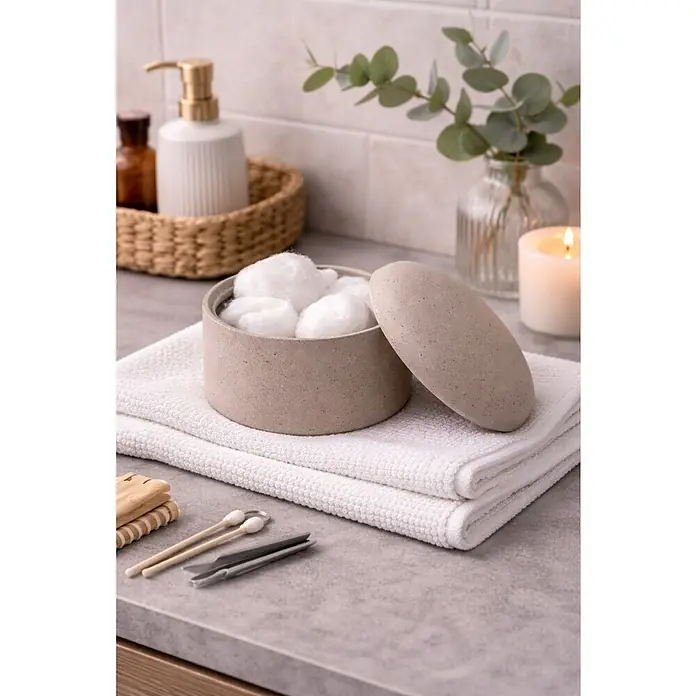 Spirella Gemma Organizador - Tierra - Recipiente jaspeado beige con tapa, lleno de bolas de algodón blancas, sobre toallas blancas entre accesorios de baño.