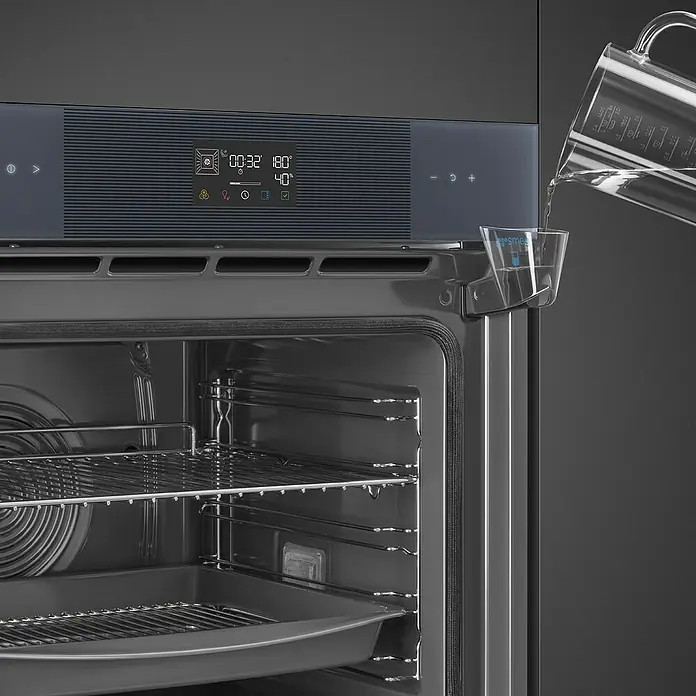 Smeg Horno empotrado SOP6102S2PG - Número de tipos de calentamiento: 12 ud., Volumen horno: 68 l - Horno encastrable gris oscuro con puerta abierta; se vierte agua en una taza humidificadora en el marco. La pantalla digital muestra ajustes.