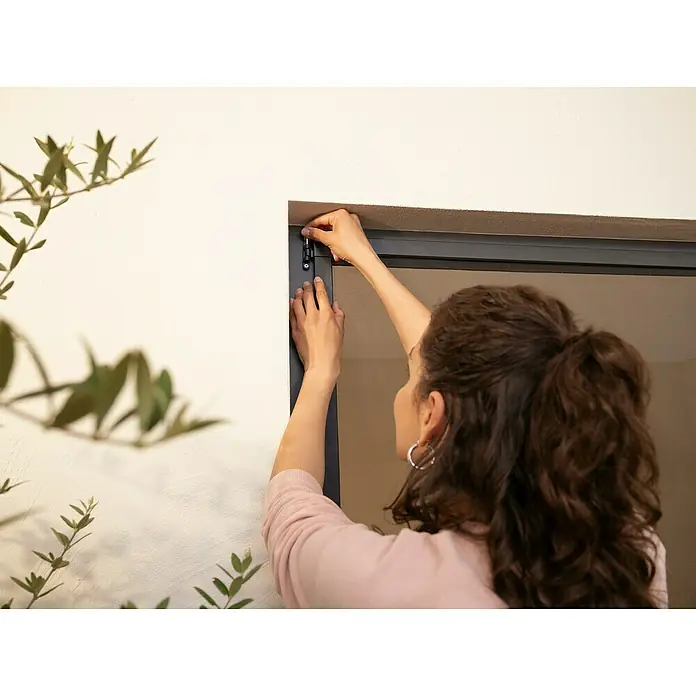 Tesa Insektenschutztür - B x H: 1,2 x 2,4 m, Weiß, Montage Insektengitter: Schrauben - Person montiert beiges Netzgitter mit dunklem Rahmen in einen Tür- oder Fensterrahmen und justiert ein oberes Scharnier.