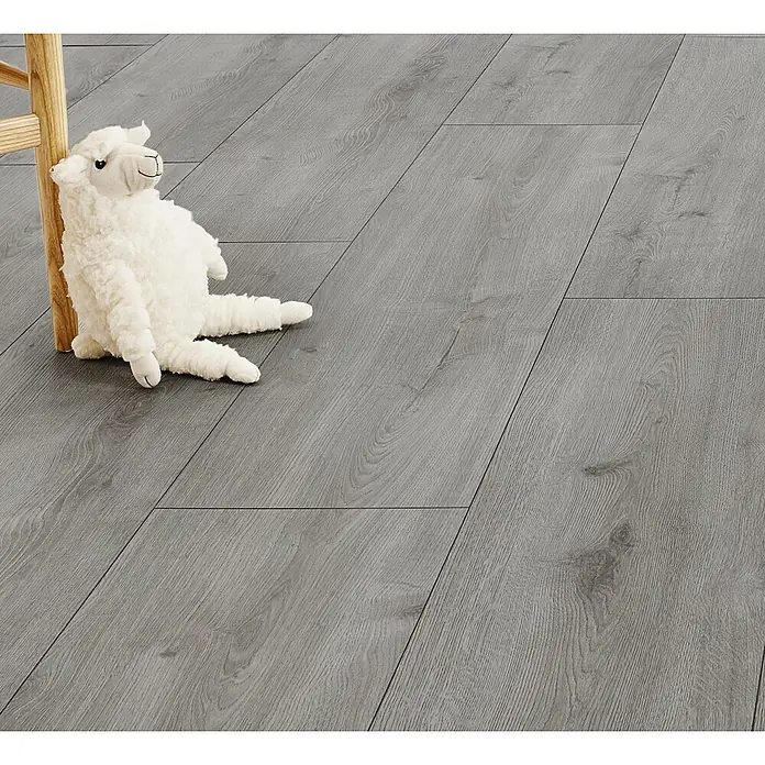 LOGOCLIC Vinto Laminat - Eiche Calais, Landhausdiele, 1.288 x 330 x 8 mm - Grauer Laminatboden mit Holzmaserung, gezeigt mit weißem Plüschtier und Holzmöbelbein, deutet auf Wohnambiente hin.