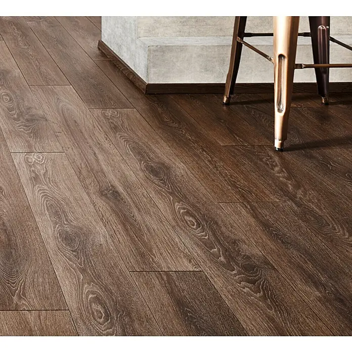 LOGOCLIC Ambienta Laminat - Eiche Oriolo, Landhausdiele, 1.288 x 195 x 10 mm - Dunkelbrauner Laminatboden in Holzoptik mit deutlicher Maserung, verlegt in einem Raum mit Betonwand und Möbeln.