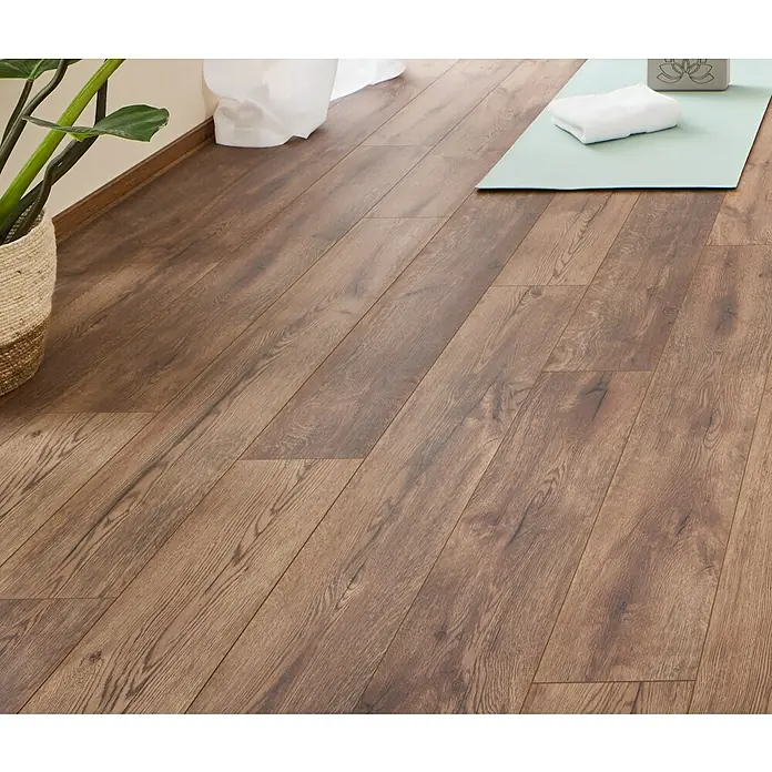 LOGOCLIC Ambienta Laminat - Eiche Mirandola, Landhausdiele, 1.288 x 195 x 10 mm - Warmbrauner Holzoptik-Boden in einem Raum, mit Pflanze und Yogamatte sichtbar.