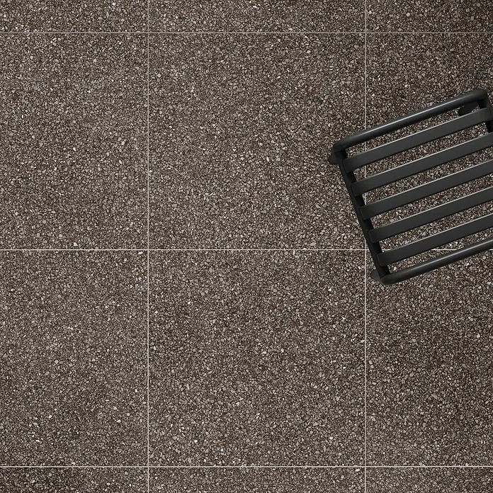 DryTile Feinsteinzeugfliese Terrazzo Red - 60 x 60 cm, Rot, Matt - Dunkler gesprenkelter Terrazzoboden mit teilweise sichtbarem schwarzem Lattenstuhl.