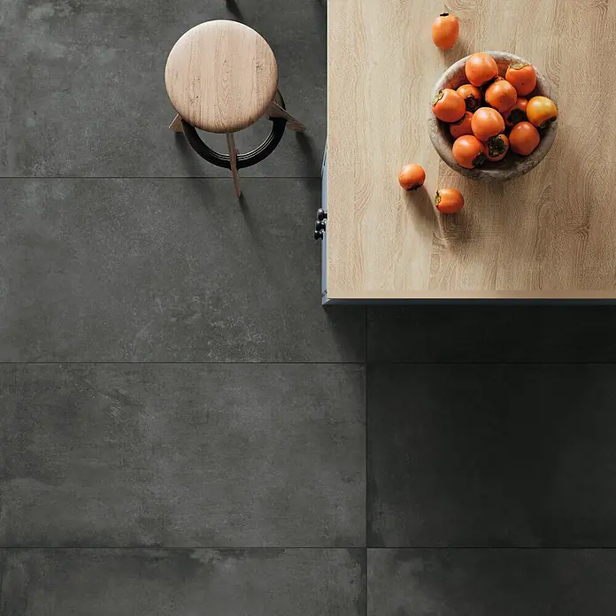 DryTile Feinsteinzeugfliese Studio Asphalt - 60 x 120 cm, Anthrazit, Matt - Dunkelgraue, rechteckige Bodenfliesen in Betonoptik, die eine schlichte, moderne Basis für einen Küchenbereich mit Holzmöbeln bilden.