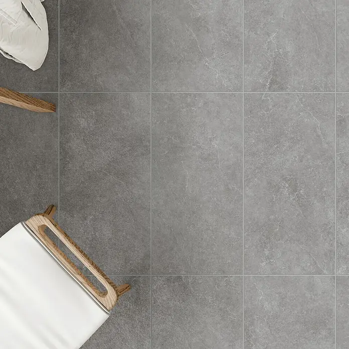 DryTile Feinsteinzeugfliese Silkstone Schlamm - 60 x 120 cm, Grau, Matt - Grauer Marmor-Effekt-Fliesenboden mit Fugen, mit Teilen eines weißen Textils und Holzmöbeln.