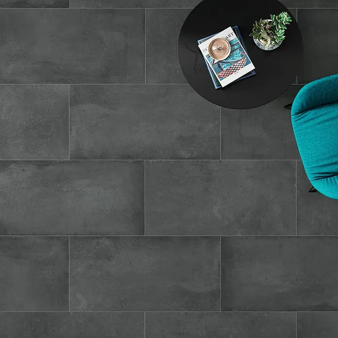 DryTile Feinsteinzeugfliese Studio Asphalt - 30 x 60 cm, Anthrazit, Matt - Dunkelgraue, rechteckige Bodenfliesen mit feiner Betonoptik, verlegt in einem Wohnraum mit Möbeln.