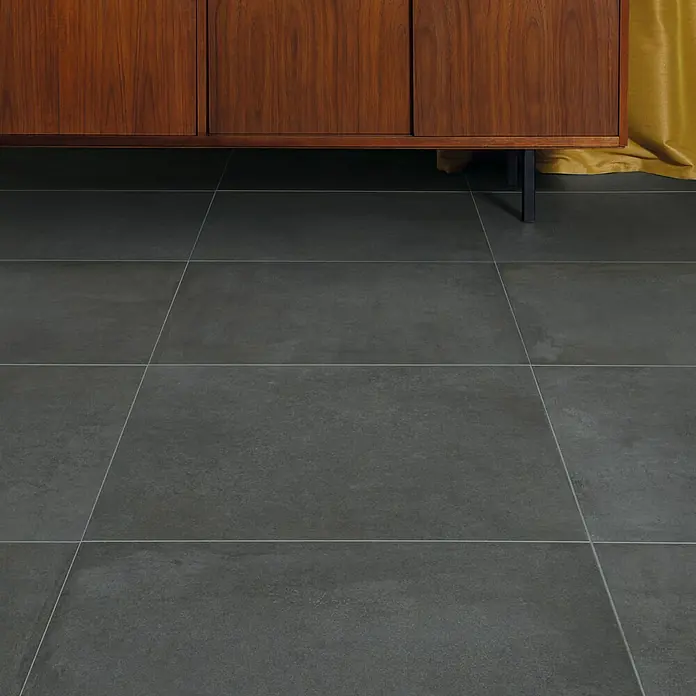 DryTile Feinsteinzeugfliese Studio Asphalt - 60 x 60 cm, Anthrazit, Matt - Dunkelgraue Bodenfliesen unter einem Holzschrank, mit Textur und Fugen.