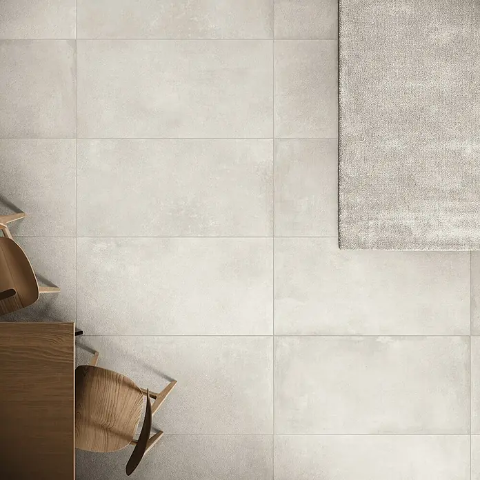 DryTile Feinsteinzeugfliese Studio Lime - 60 x 120 cm, Beige, Matt - Heller grauer Fliesenboden mit strukturiertem Teppich und Teilen von Holzmöbeln.