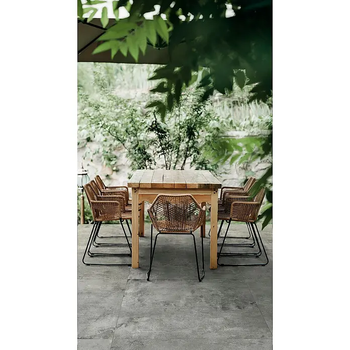 Feinsteinzeugfliese Urban - 60 x 120 cm, Grey, Matt - Hölzerner Gartentisch mit braunen Korbstühlen auf einer Terrasse, umgeben von grünem Blattwerk.