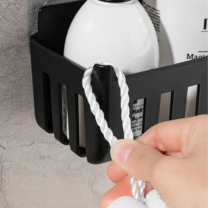 Cesta de baño Molly - 11 x 25 x 9 cm, Plástico, Negro - Cesta de ducha negra con botellas y un gancho lateral del que una mano sujeta una cuerda blanca.