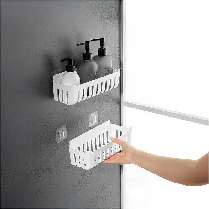 Cesta de baño Molly - 11 x 25 x 9 cm, Plástico, Blanco - Cesta de ducha de plástico blanco, una montada con botellas, otra sostenida por una mano, mostrando ganchos adhesivos.