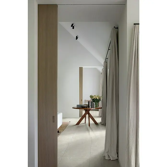 Feinsteinzeugfliese Cortina - 60 x 120 cm, Bianco, Matt - Helle Diele mit rundem Holztisch, Blumenarrangement und sanften beigen Vorhängen.