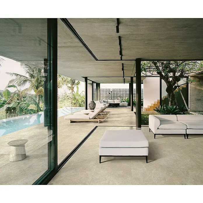 Feinsteinzeugfliese Chalk Sallow - 120 x 120 cm, Beige, Matt - Großformatige, hellbeige Fliesen in Steinoptik bedecken den Boden eines modernen Wohnraums, der sich zur Poolterrasse erstreckt.