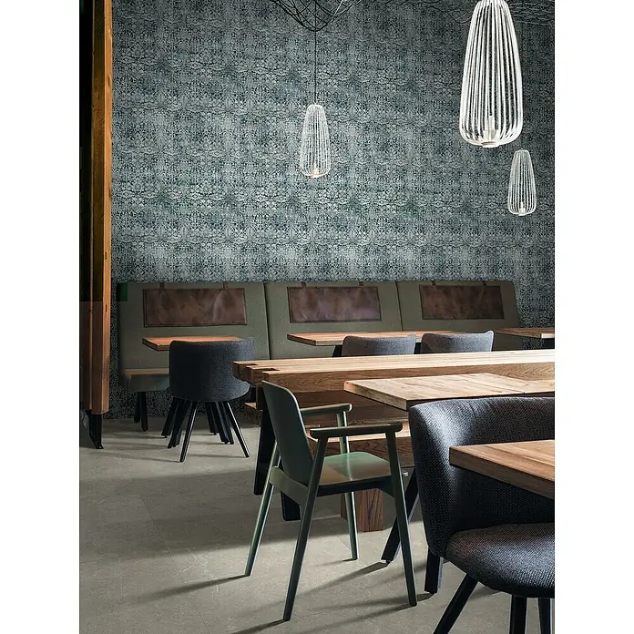 Feinsteinzeugfliese Chalk Stone Grig - 60 x 120 cm, Grig, Matt - Blaugrüne gemusterte Tapete mit Used-Look an einer Restaurantwand hinter Sitzbänken.