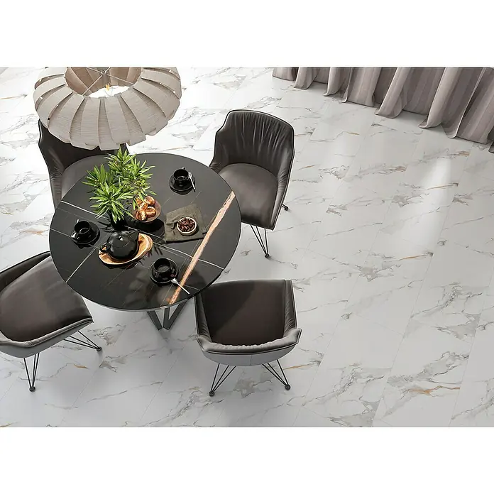 Suelo vinílico SPC Calacatta Gold - 94 cm x 47 cm x 5 mm, Baldosa, Blanco - Azulejos de mármol blanco con vetas grises y doradas en un comedor con mesa redonda y sillas.