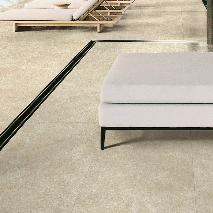 Feinsteinzeugfliese Chalk Sallow - 120 x 120 cm, Beige, Matt - Beige Outdoor-Fliesen und schwarzer Linienablauf auf einer Terrasse mit Loungemöbeln.